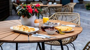 Une table ronde en bois, sur laquelle sont disposés des aliments pour le petit-déjeuner, notamment une assiette de pâtes, un verre de jus d’orange, une théière et un bol de confiture.