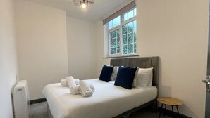 Ein Schlafzimmer mit einem Bett, Kissen, einem kleinen Tisch und einem Fenster.