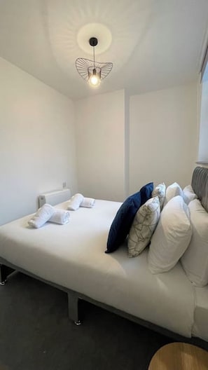 A single bed with white bedding, a bedside table, and a unique ceiling light fixture.