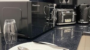 Eine Küche mit einer schwarzen Mikrowelle, einem Glas, einem Teller mit Besteck und einem Toaster.