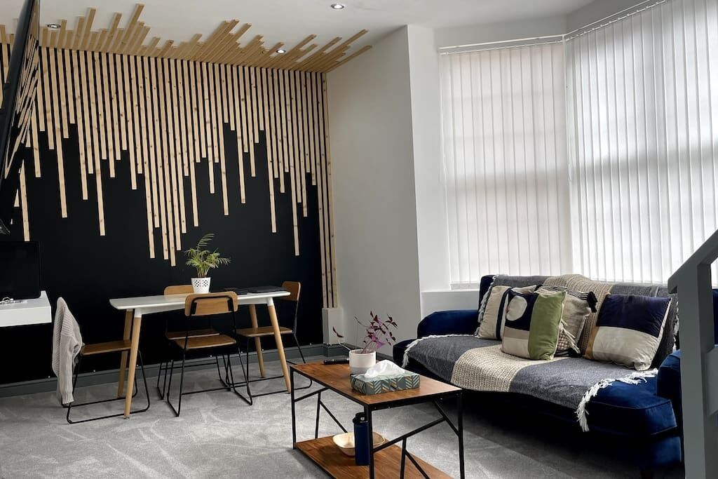 A modern living room with a black wall, wooden slats, a blue sofa, and a dining area with a table and chairs.