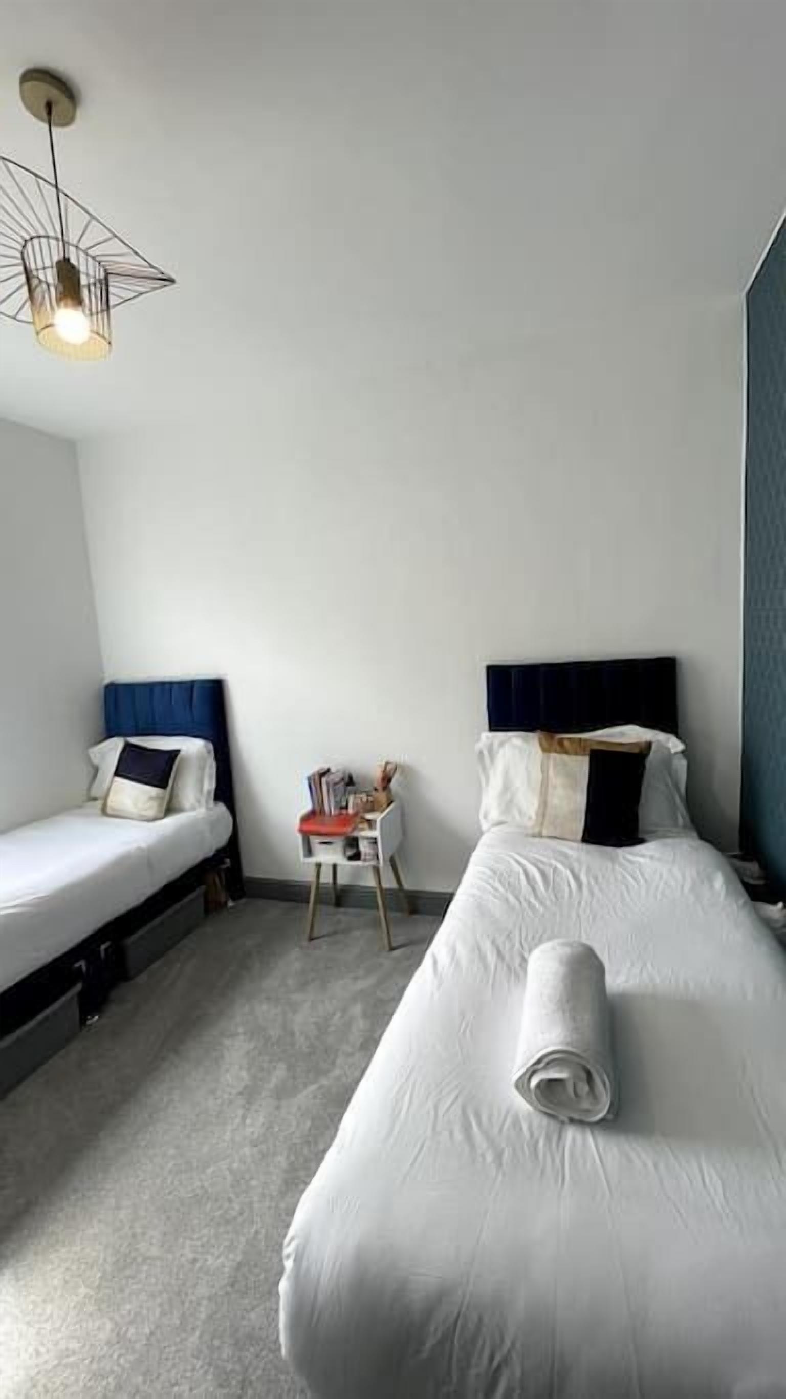 Hotellihuone, jossa on kaksi erillistä sänkyä, pieni pöytä, tuoli ja kattovalaisin.