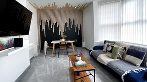 Ein modernes Wohnzimmer mit einem Flachbildfernseher, einem Couchtisch aus Holz, einer Couch mit Kissen und einem Essbereich mit Tisch und Stühlen.