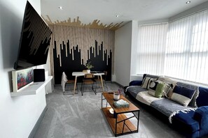 A modern living room with a sofa, coffee table, TV, and a unique wall design.