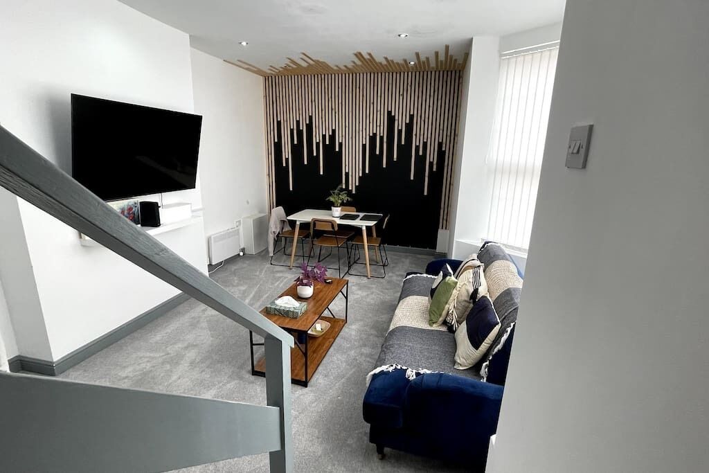 Ein modernes Wohnzimmer mit Flachbildfernseher, einem Essbereich mit Tisch und Stühlen sowie einem blauen Sofa.