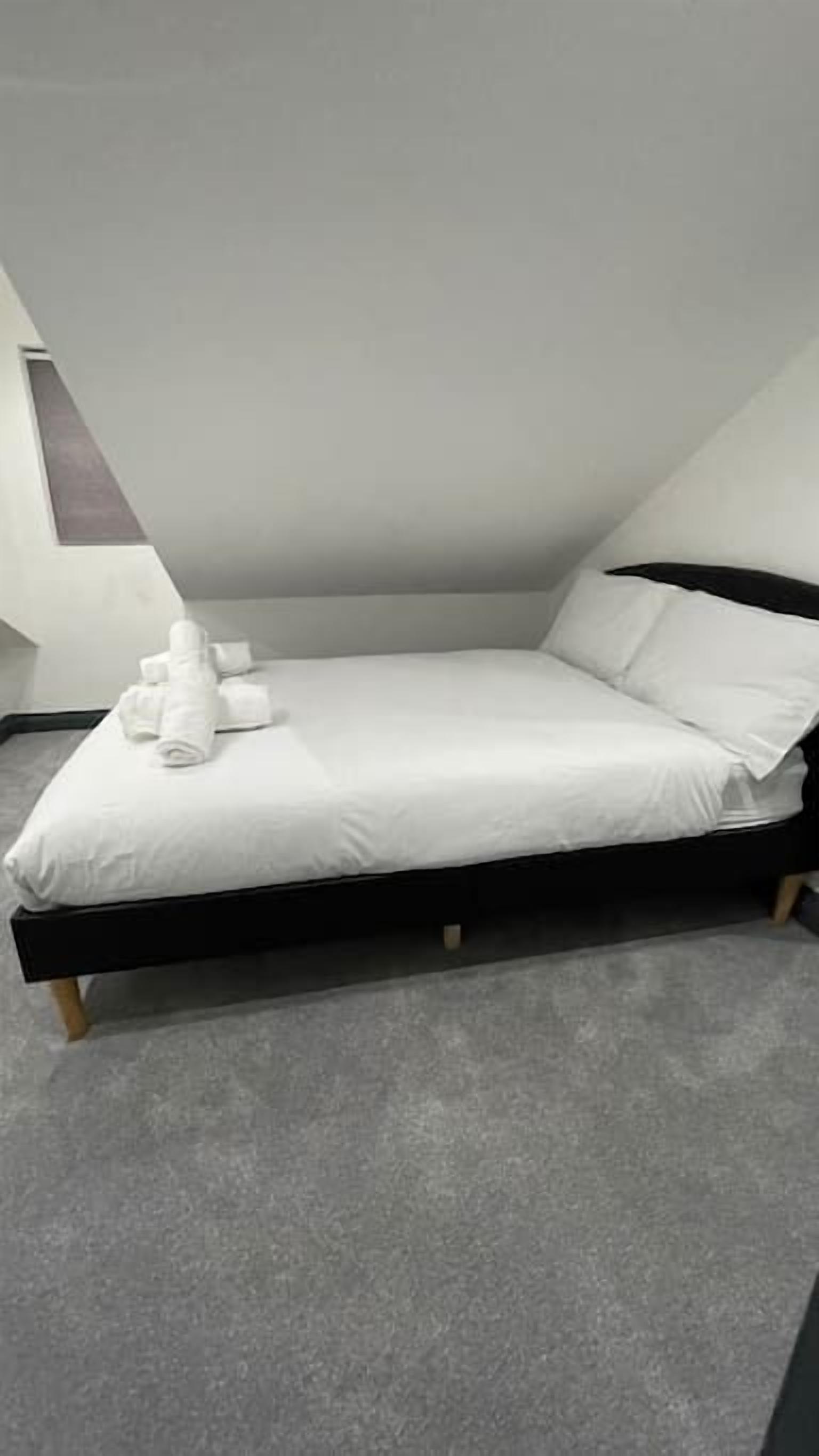 Une chambre moderne avec un lit simple, un cadre noir, du linge de lit blanc et un tapis gris.