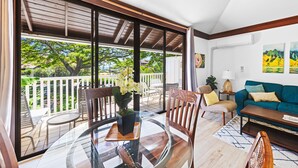 Un salon moderne avec une table en verre, des chaises en bois, un canapé et un balcon offrant une vue sur les arbres et une clôture blanche.