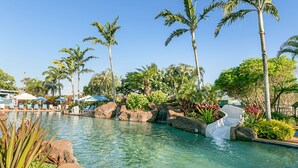 Une piscine aux eaux cristallines, agrémentée d’une cascade, entourée de palmiers et de chaises longues.