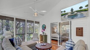 A spacious living room with a large sofa, a coffee table, and a view of a garden through large windows.