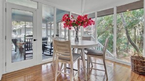 A room with a round table, four chairs, and a vase with pink flowers.