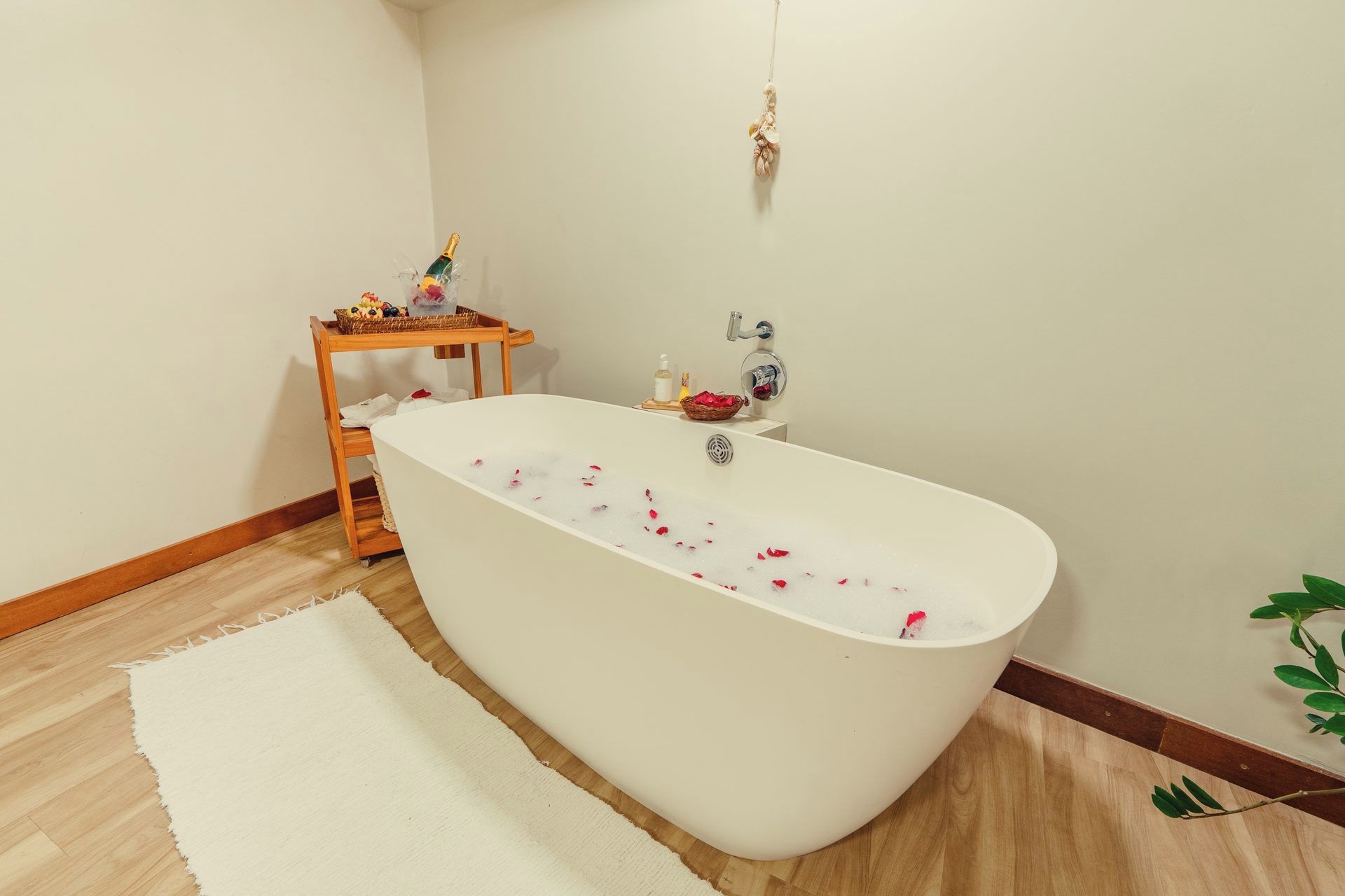 Un baño moderno con una bañera independiente, una mesita de madera con una cesta de frutas y un adorno colgante.