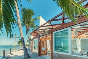 A beachfront property with a wooden deck, a glass-enclosed room, and a sign reading 'AQUA'. - AQUA BY SAMBASS (Cairu)