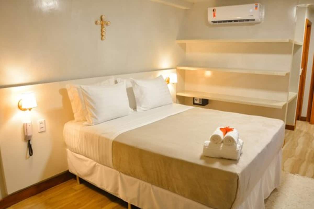 A hotel room with a bed, bedside lamp, air conditioning unit, and a phone on the wall.