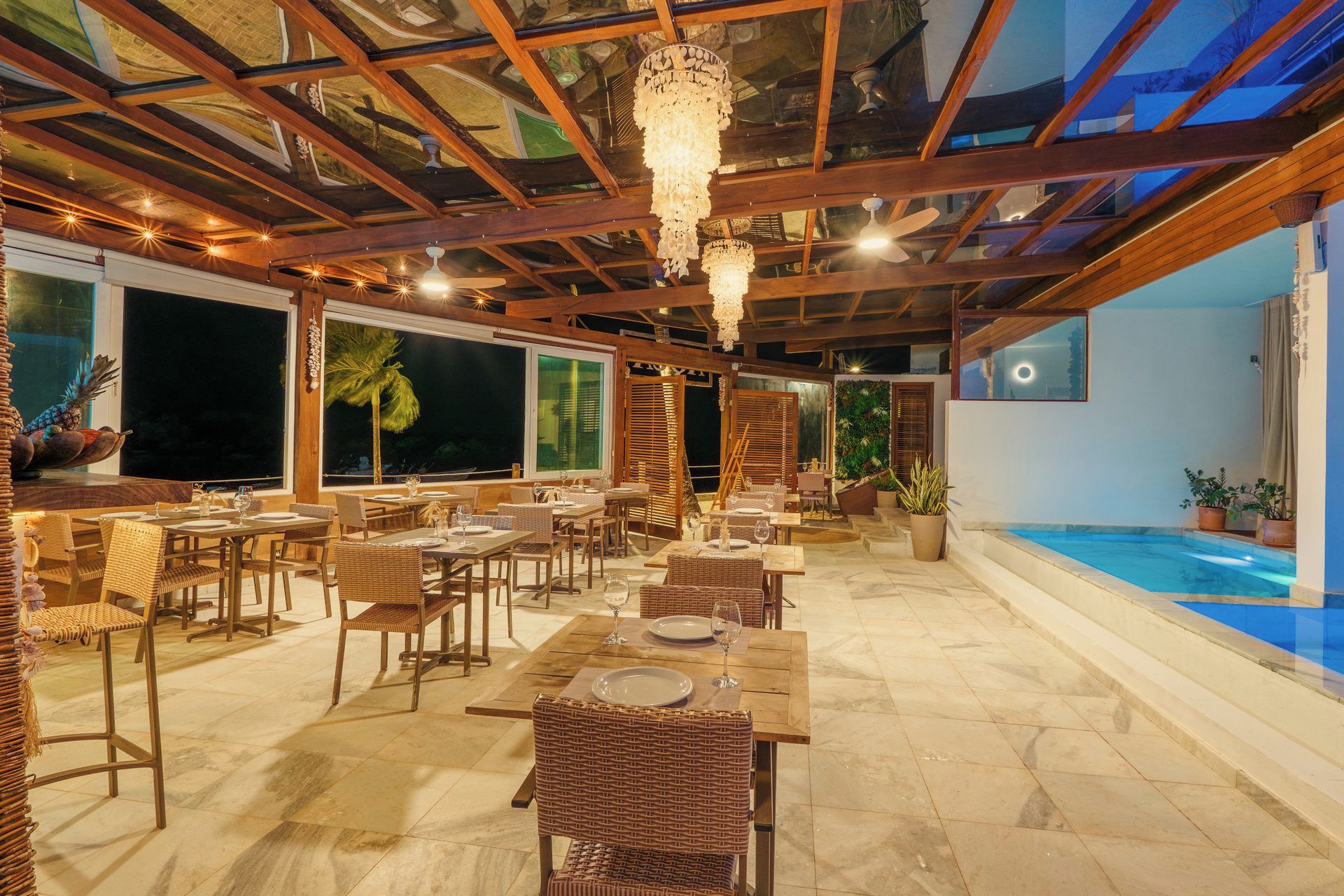 An outdoor dining area with wooden tables and chairs, a pool, and a view of the night sky.