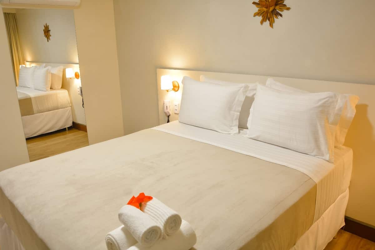 A hotel room with a large bed, two bedside lamps, and a mirror.