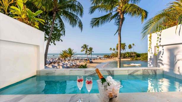 A poolside view with a clear view of the beach and ocean, two glasses of champagne, and a bucket of ice with a bottle. - AQUA BY SAMBASS (Cairu)