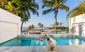 A poolside view with a clear view of the beach and ocean, two glasses of champagne, and a bucket of ice with a bottle. - AQUA BY SAMBASS (Cairu)