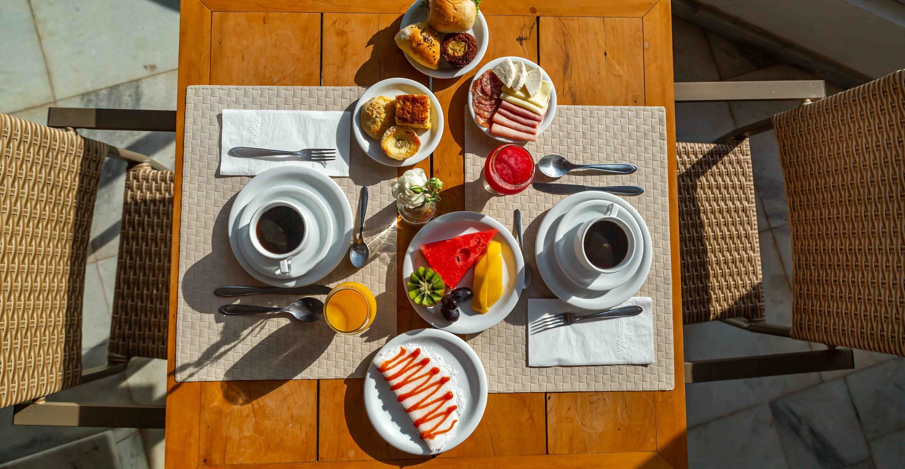 Een ontbijttafel gedekt met borden eten, koffiekopjes en een glas sinaasappelsap.