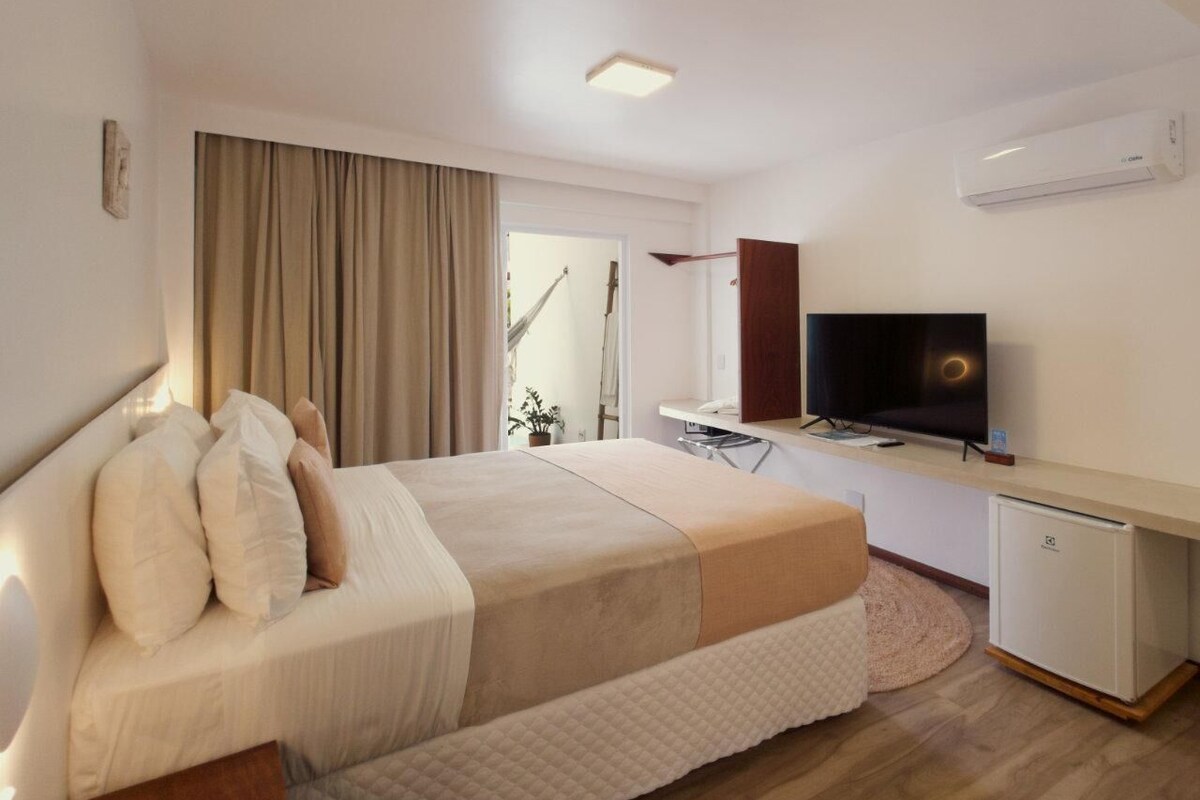 A hotel room with a bed, a television, a desk, and a small refrigerator.