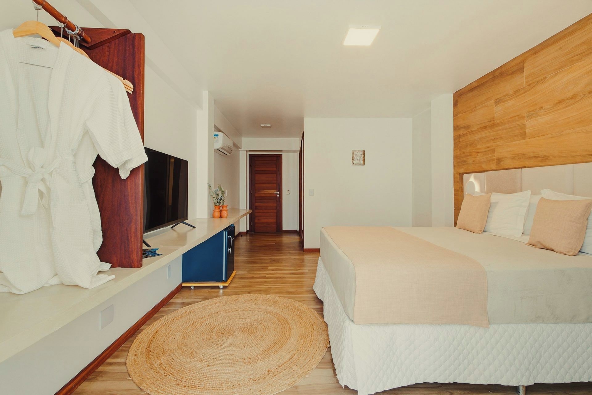 Un dormitorio con cama, televisor, cabecera de madera y baño a la vista.