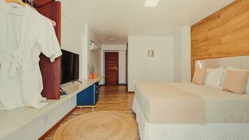 A bedroom with a bed, a TV, a wooden headboard, and a bathroom visible in the background.