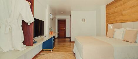 Un dormitorio con cama, televisor, cabecera de madera y baño a la vista.