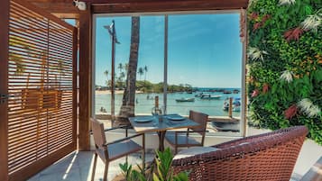 An outdoor seating area with a view of the sea, featuring a table, chairs, and a wooden pergola.