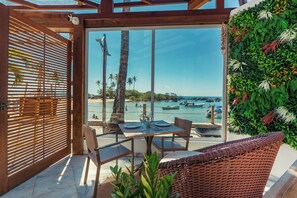 An outdoor seating area with a view of the sea, featuring a table, chairs, and a wooden pergola. - AQUA BY SAMBASS (Cairu)