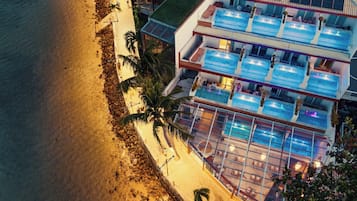 A multi-story building with a pool area, a beach, and palm trees.