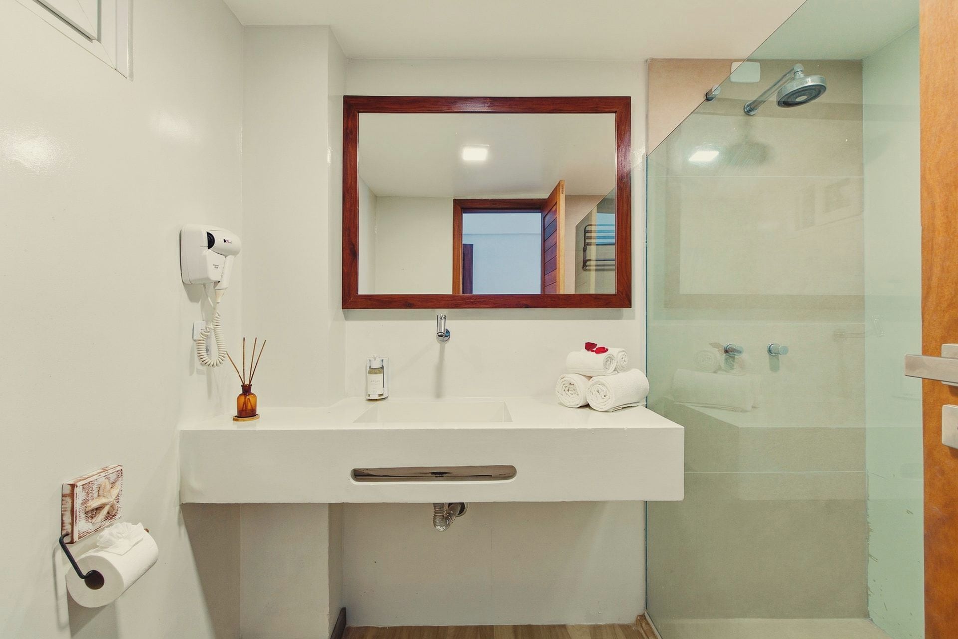 A bathroom with a white sink, a mirror, a hairdryer, a towel rack, and a shower.