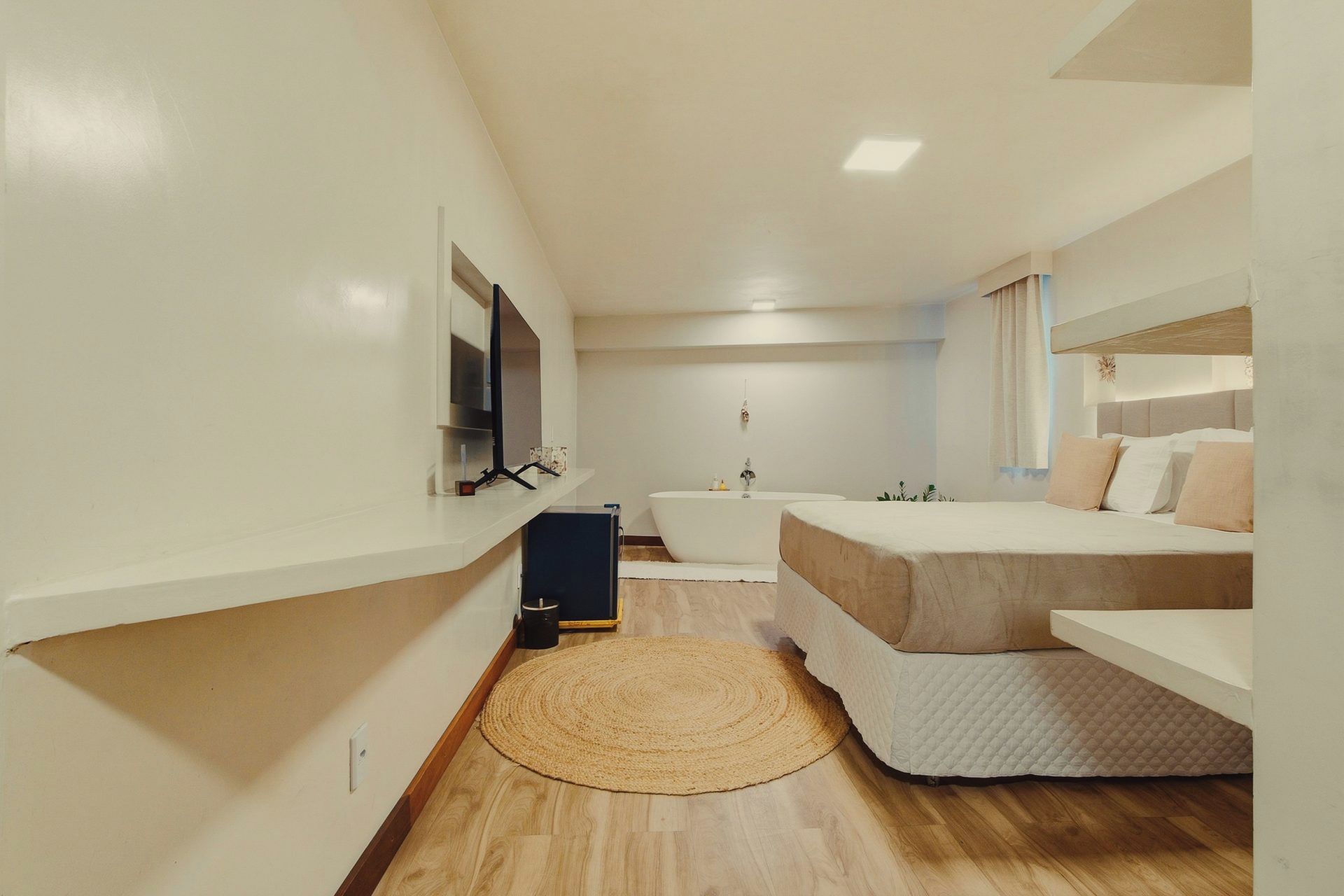 A compact hotel room with a bed, a small bathroom with a bathtub, and a television on the wall.