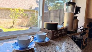 Una cucina con una macchina da caffè, due tazze su un piattino e un cartello con scritto 'Coffee Bar'.