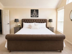 A large, tufted bed with white linens, two bedside tables with lamps, a chandelier, and a door.