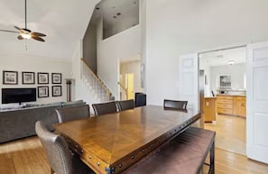 A spacious dining area with a long wooden table, leather chairs, and a modern ceiling fan.