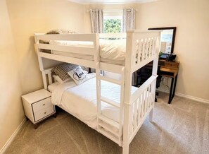 Un lit superposé avec une table de chevet, un bureau et une fenêtre avec des rideaux.
