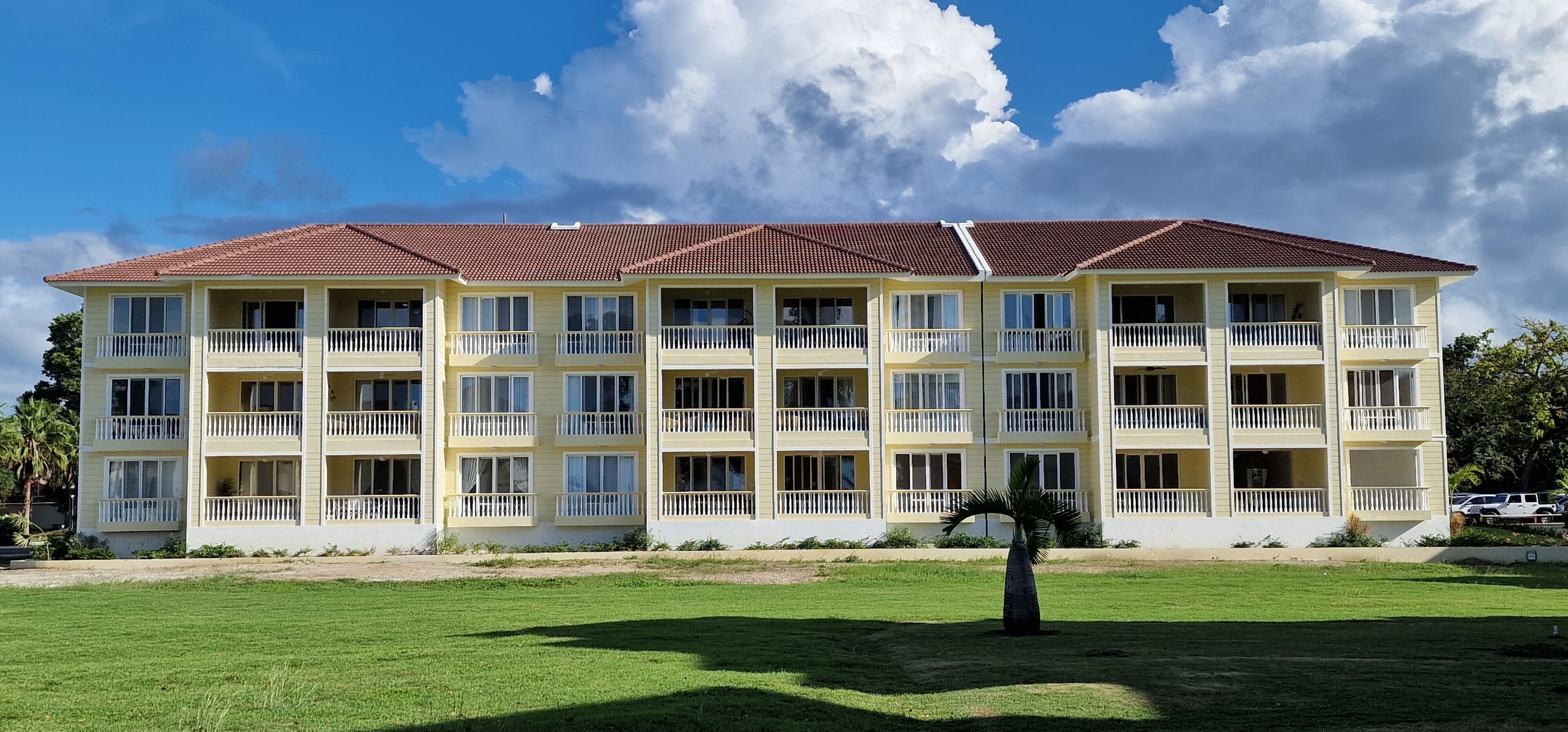 A multi-story hotel with a red-tiled roof, balconies, and a well-maintained lawn.