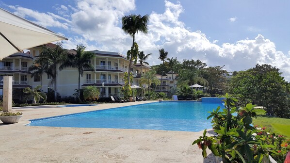 A hotel with a swimming pool, palm trees, and a clear sky.
