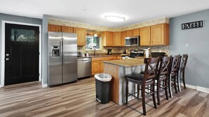 A modern kitchen with wooden cabinets, stainless steel appliances, and a bar area with stools.