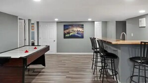 A room with a pool table, bar area, and a painting on the wall.