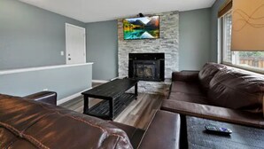 A living room with a stone fireplace, a television mounted above it, and a leather sofa.
