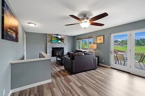 A spacious living area with a fireplace, a ceiling fan, and a view of the outdoors through large sliding doors.