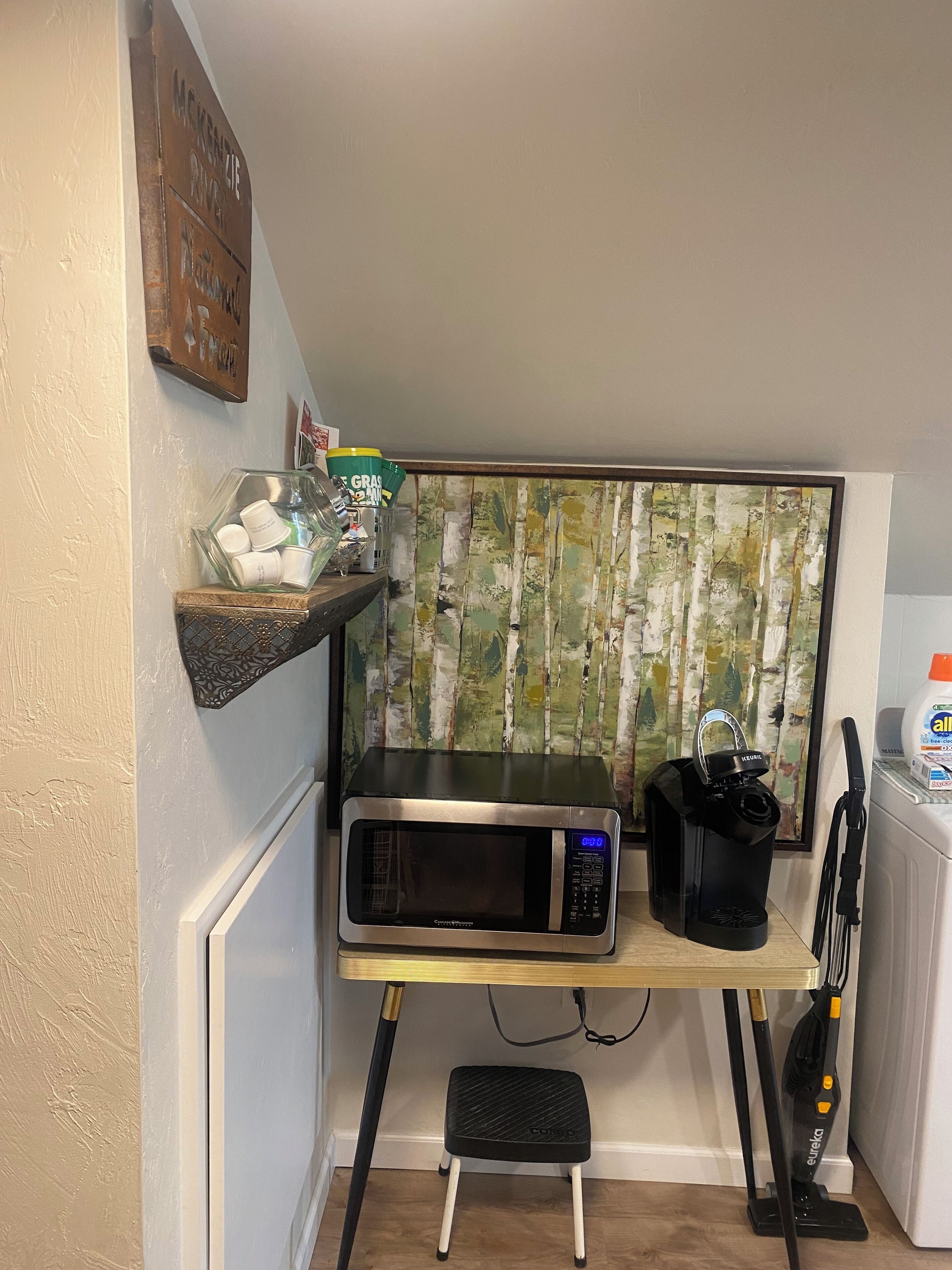 A compact kitchenette with a microwave, a step stool, and a vacuum cleaner.