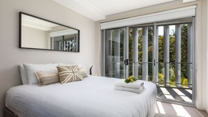 A bedroom with a large bed, a mirror, and a view of greenery through a sliding glass door. - Husqi Loft - by Latitiude South Coast (Huskisson)