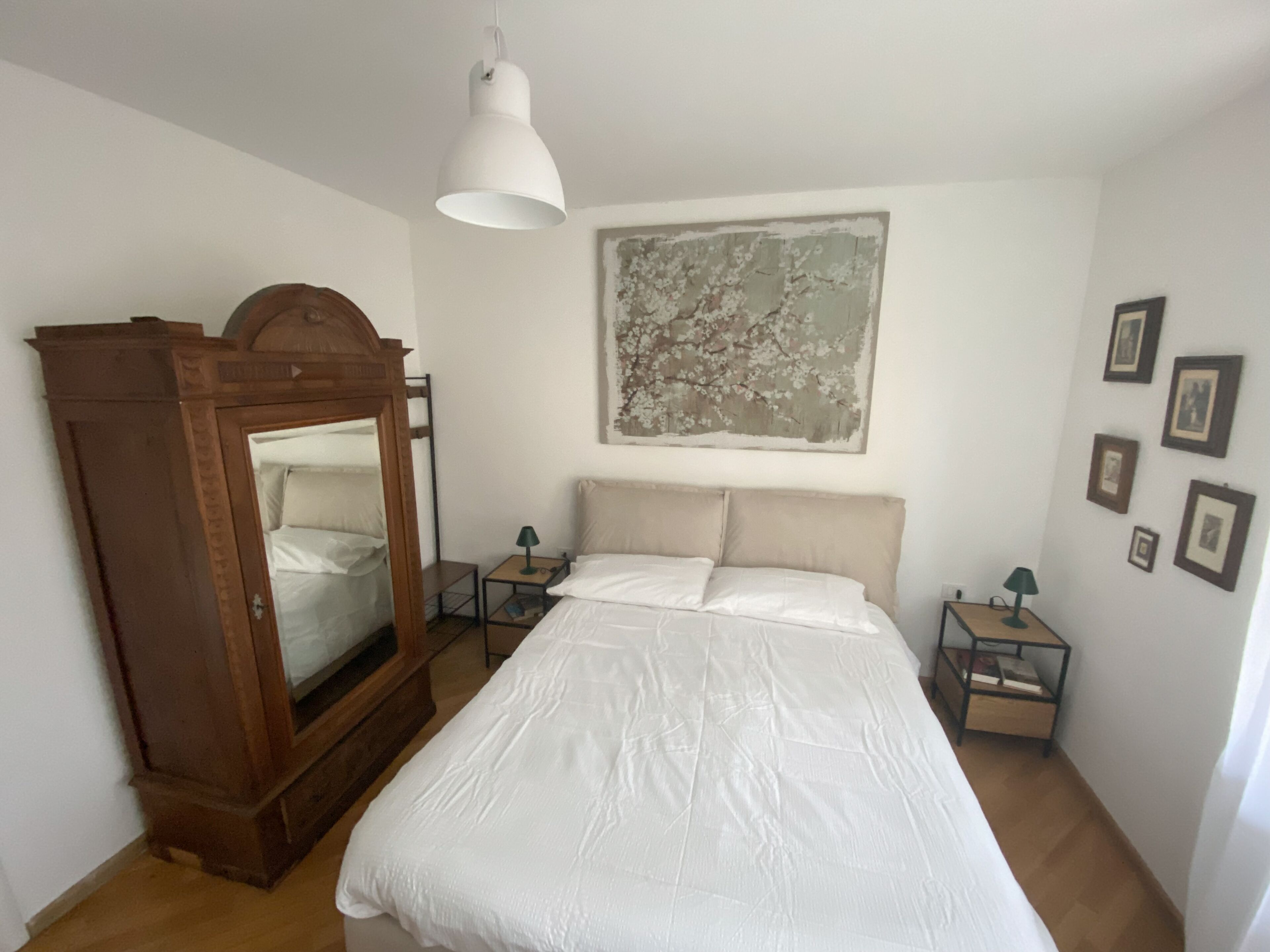 Ein Schlafzimmer mit einem großen Bett, einem Holzschrank, einem Nachttisch, einer Lampe und einem Wandbild.