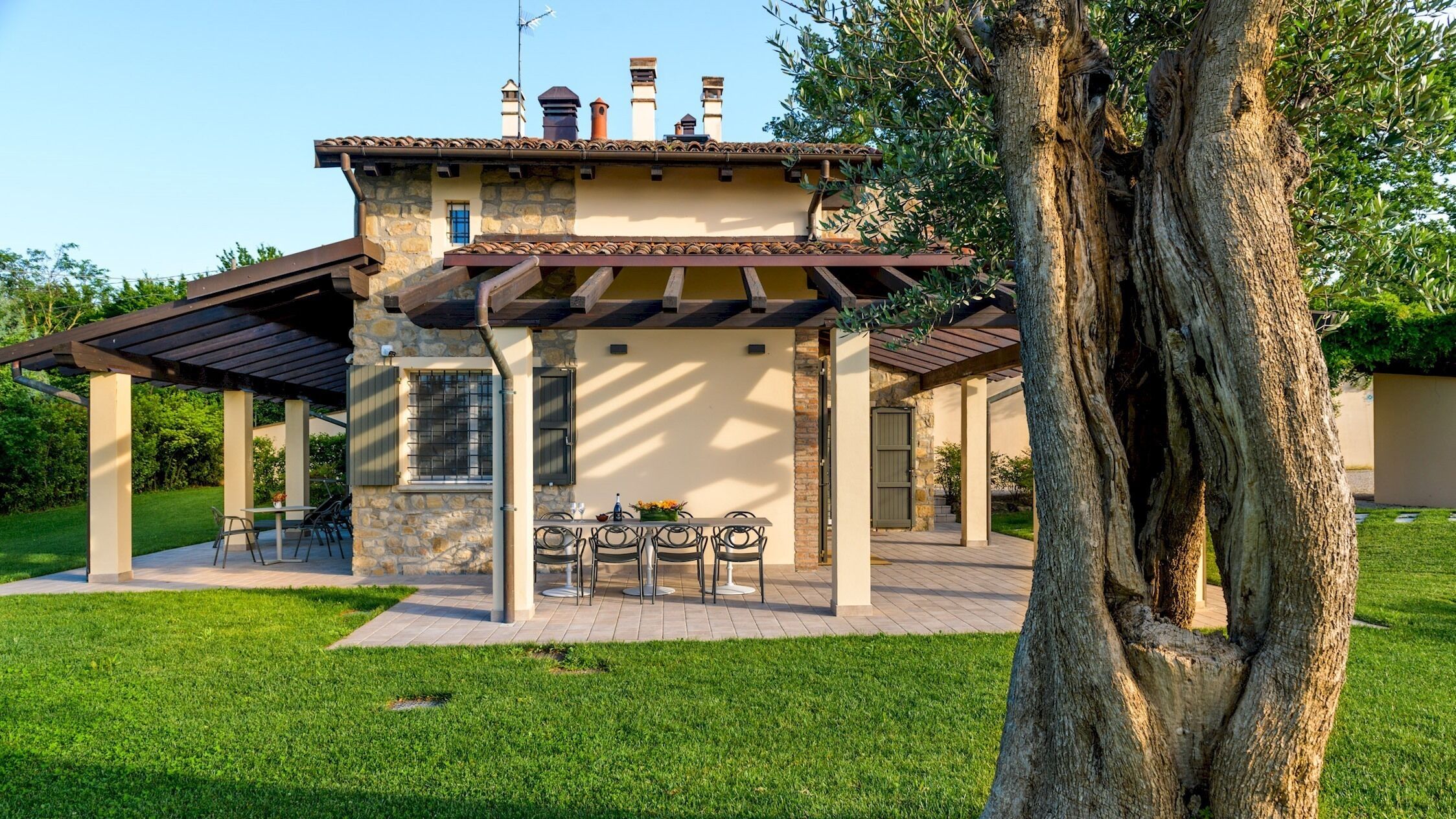 Une maison en pierre avec un patio, un espace salon extérieur et un grand arbre.
