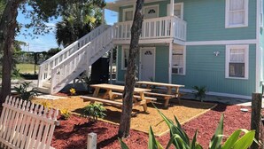 Uma casa de dois andares com varanda, deck de madeira e mesa de piquenique.