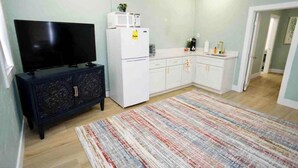 A compact kitchen with white cabinets, a black entertainment unit, and a colorful striped rug.
