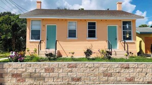 A two-story house with a stone foundation, a flat roof, and a front porch with steps.
