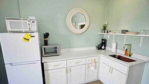 A compact kitchen with white cabinets, a microwave, a toaster, a sink, and a round mirror on the wall.