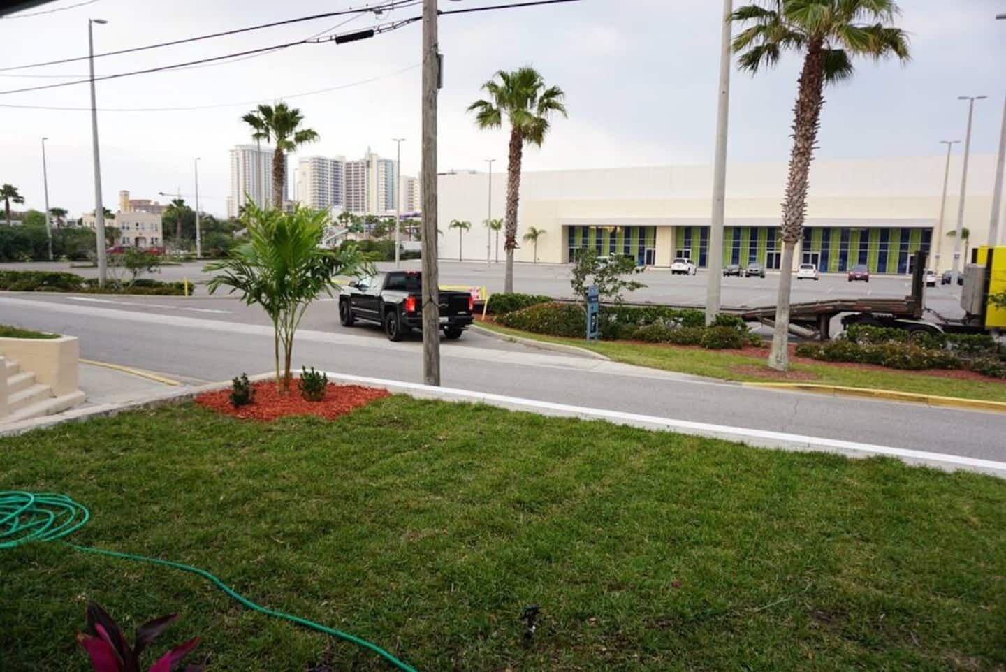 A street view with a building, palm trees, and a parked truck.